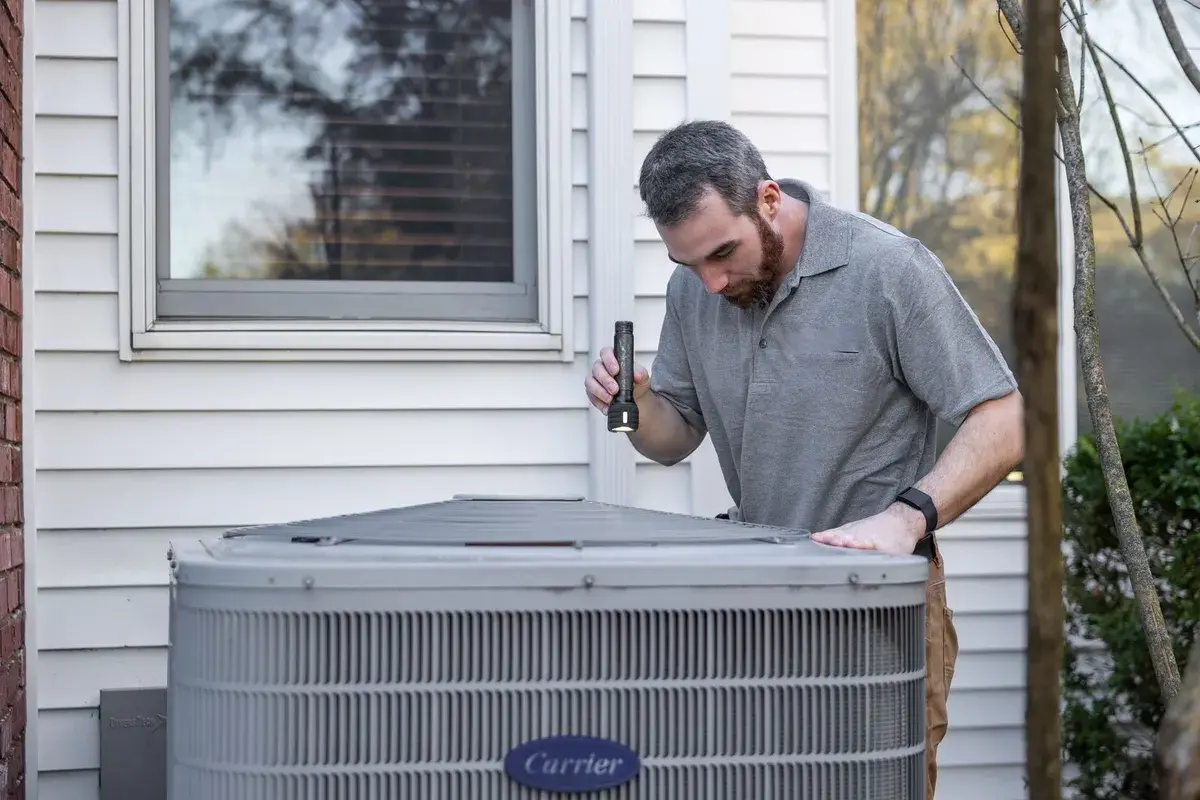 A/D technician inspecting a residential air conditioning condenser unit outside a home